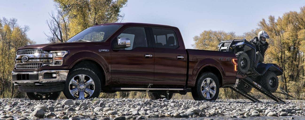 A side view of a man putting a large ATV in the bed of a 2020 Ford F-150 on a rock trail near Cincinnati, OH.