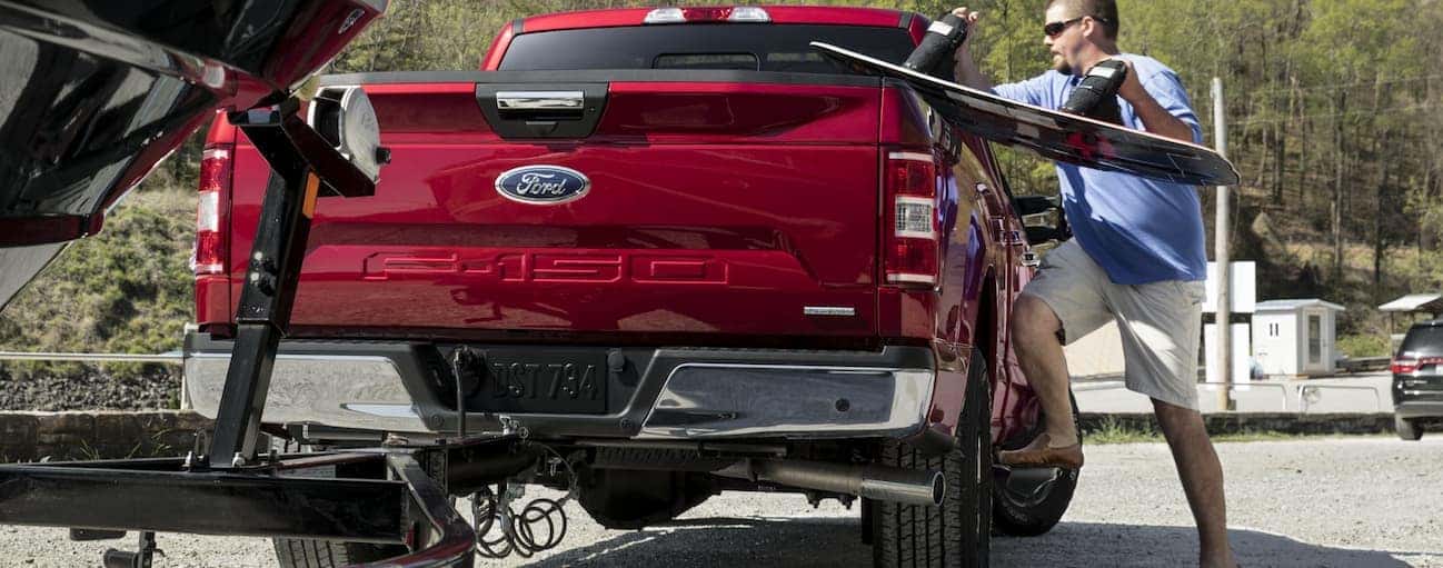 A man is loading boat equipment into the bed of his red 2020 Ford F-150 at a boat yard.