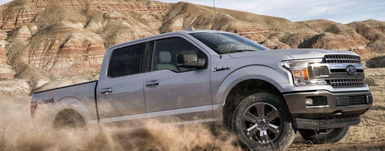 A silver 2020 Ford F-150, which wins when comparing the 2020 Ford F-150 vs 2020 Nissan Titan, is driving through a dirt pit while a dirt cloud rises.