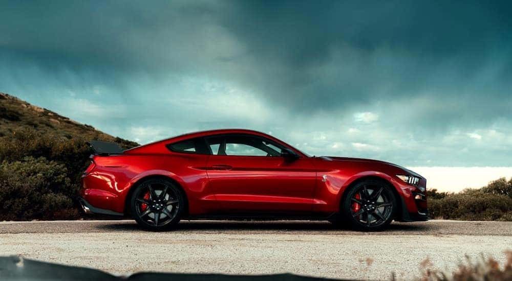 A red 2020 Ford Mustang Shelby GT 500 is shown from the side with a cloudy sky.