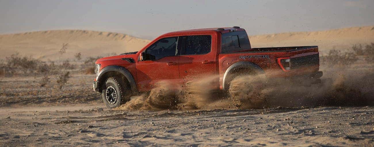 A red 2021 Ford F-150 Raptor is off-roading in dirt.