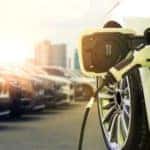 A white EV model vehicle is charging while gas vehicles are in a row next to it.