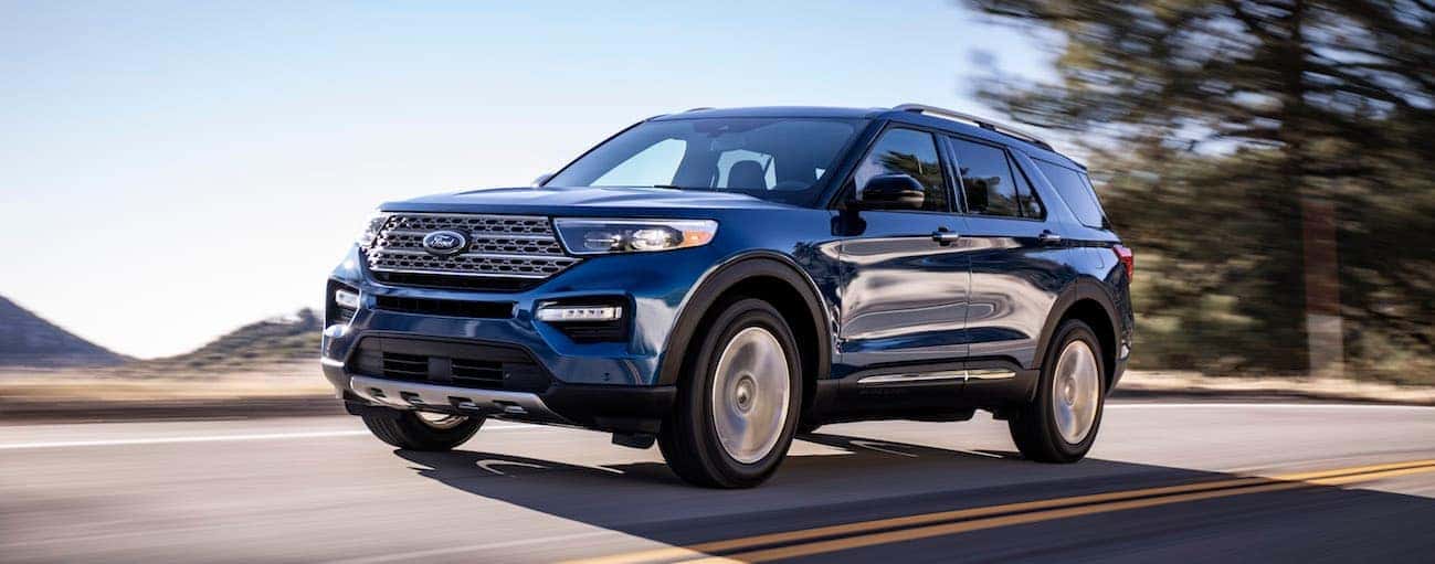 A blue 2020 Ford Explorer is driving on a road with hills in the distance. 