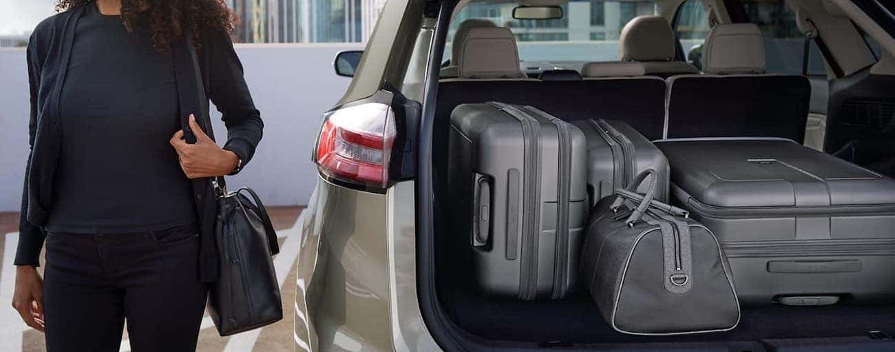 A woman is standing next to the open liftgate of her tan 2020 Ford Edge and there is luggage in the cargo area.