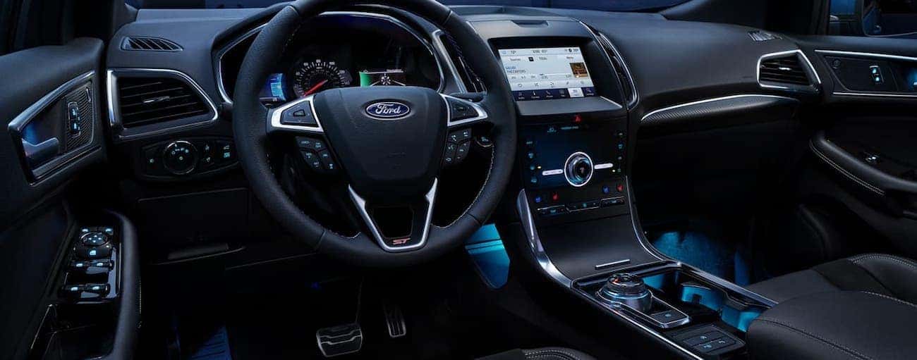 The lit up steering wheel and dashboard is shown of a 2020 Ford Edge at night.