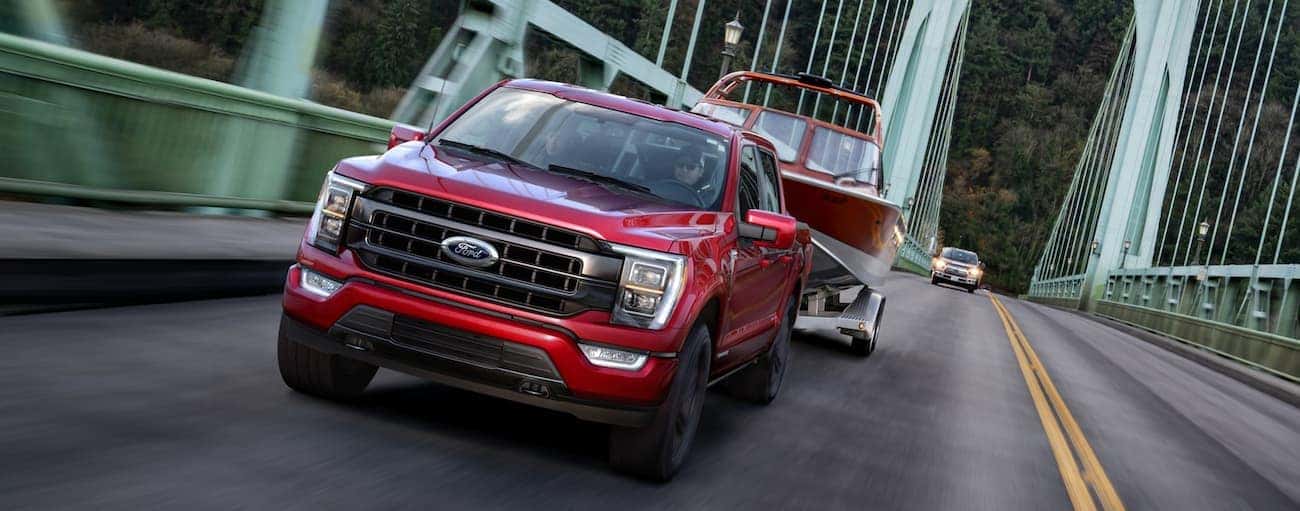 A red 2021 Ford F-150 is towing a boat over a green bridge near Cincinnati, OH.