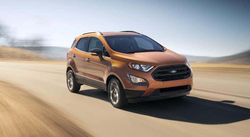 One of the popular Ford SUVs in Cincinnati, OH, an orange 2020 Ford EcoSport is driving on an empty road.