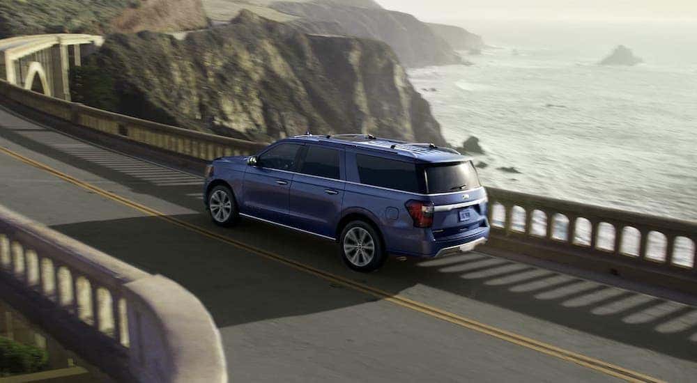 A blue 2020 Ford Expedition Platinum is driving on a coastal highway.