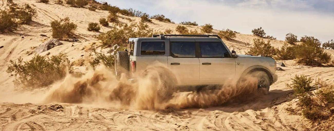A blue 2021 Ford Bronco 4-Door is driving through loose sand in the desert.