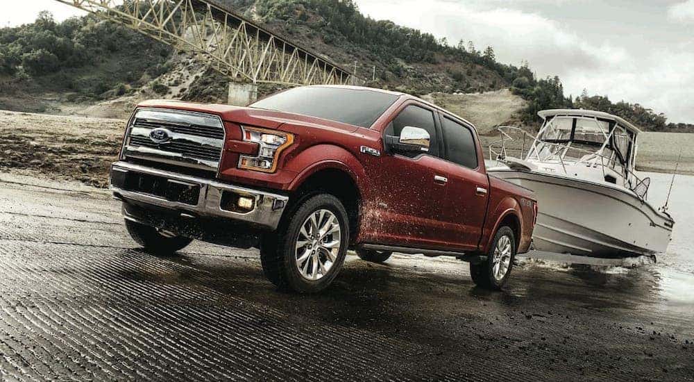 A red 2017 Ford F-150 is pulling a boat out of a river.