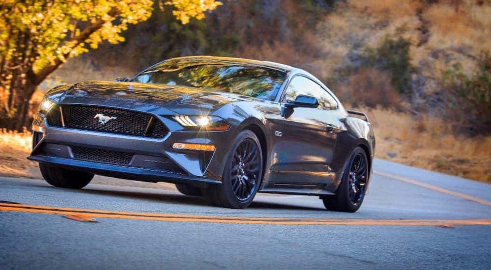 A popular used Ford for sale, a gray 2018 Ford Mustang is driving on a rural highway.