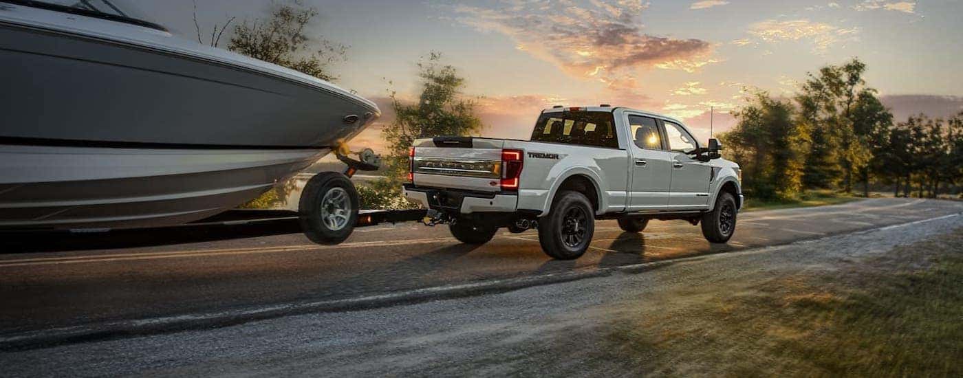 A white 2020 Ford F-250 is towing a boat at sunset on a highway near Cincinnati, OH, after winning the 2020 Ford F-250 vs 2020 Chevy Silverado 2500HD comparison.