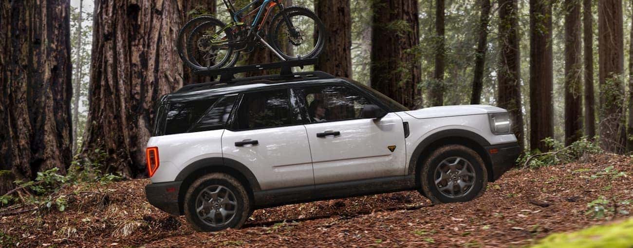 A white 2021 Ford Bronco Sport is shown from the side off-roading in the woods with bikes on the roof.