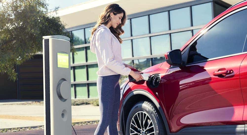 A woman is charging a red 2020 Ford Escape Hybrid.