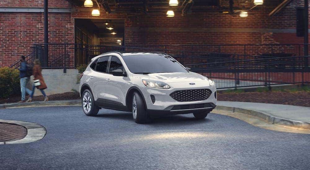 A white 2020 Ford Escape is driving in front of a brick building.