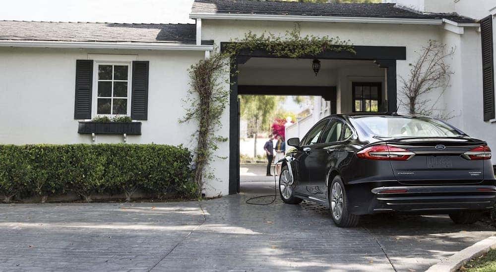 A popular Ford in Cincinnati, OH, a black 2020 Ford Fusion Hybrid, is shown charging in front of a white house.