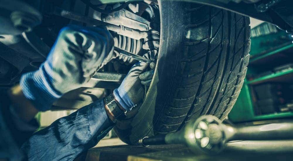 A mechanic is shown working behind the wheel while under a car.