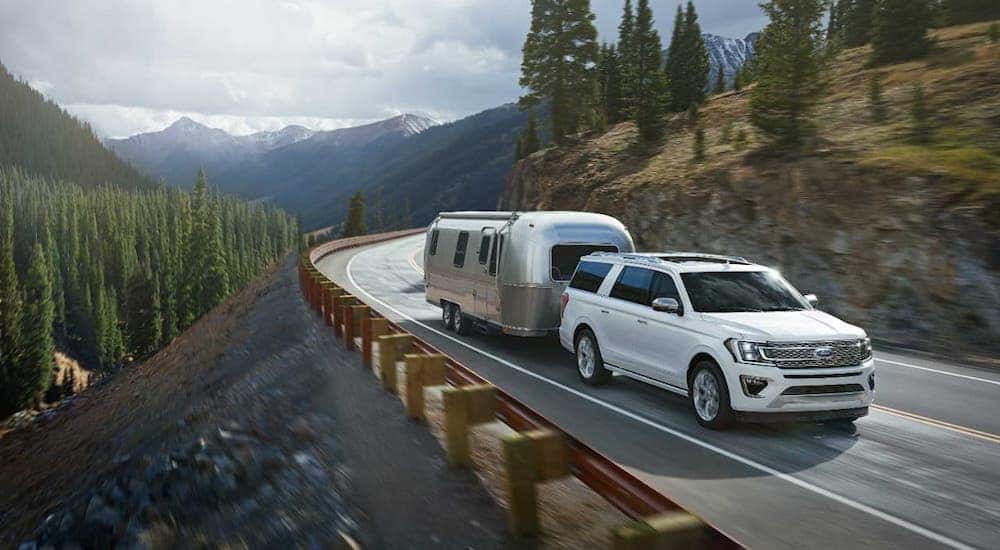 A popular used Ford for sale, a white 2018 Ford Expedition Platinum, is towing an Airstream camper trailer on a mountain road.