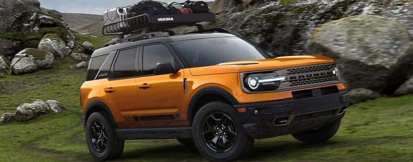 An orange 2021 Ford Bronco Sport, coming to your local Cincinnati Ford dealer, with luggage on the roof is driving around large rocks.