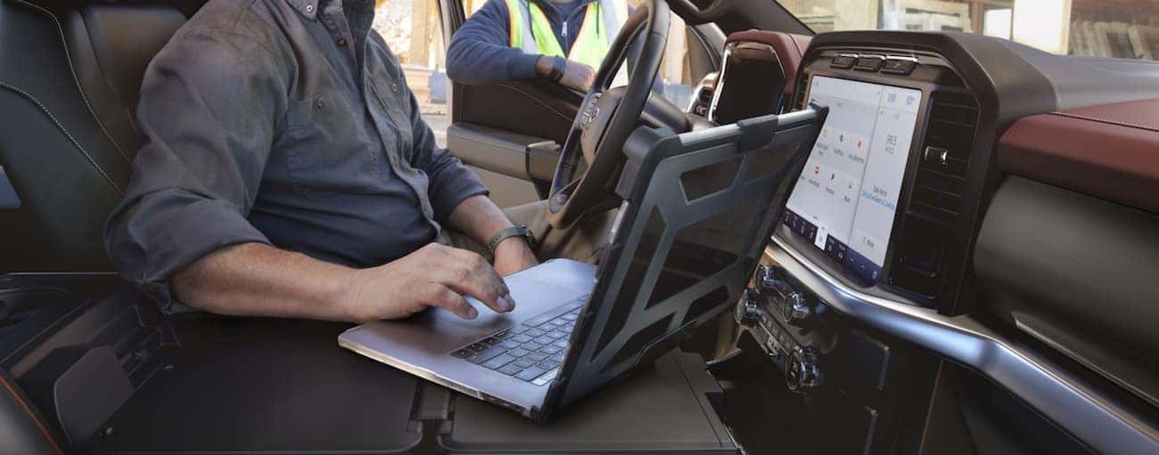 A man is in a 2021 Ford F-150 on a laptop while talking to a construction worker outside the truck.