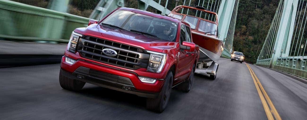 A red 2021 Ford F-150 is towing a boat across a bridge near Cincinnati, OH, after winning the 2021 Ford F-150 vs 2020 Ford F-150 comparison.