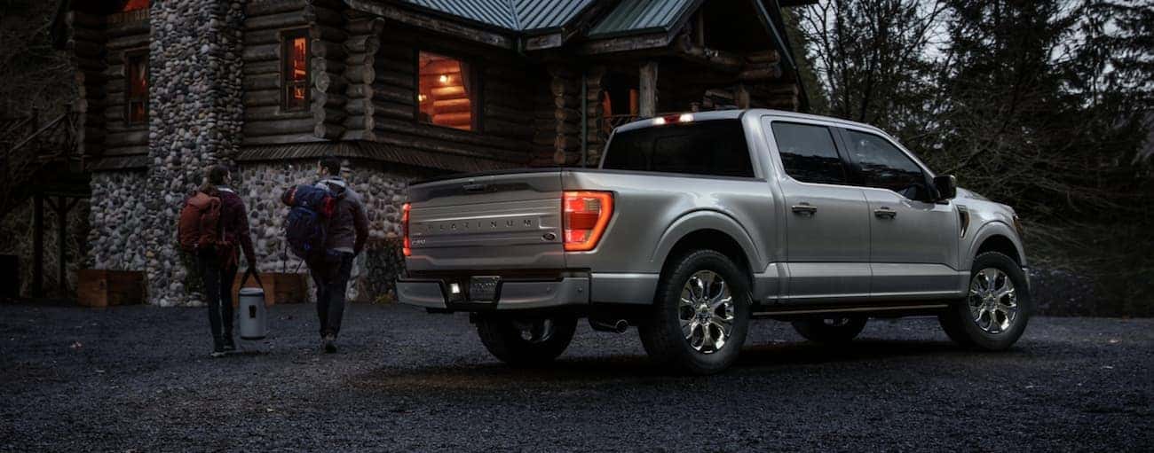 A couple is walking to a cabin at night with a silver 2021 Ford F-150 parked outside.