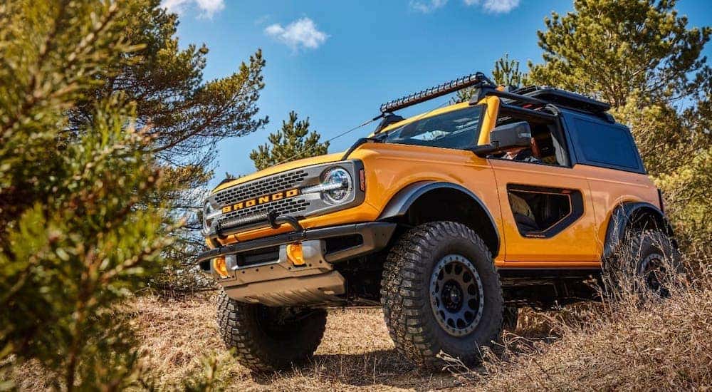 The newest to the Ford SUV lineup, a yellow 2021 Ford Bronco 2-door is shown from the side driving on a trail near Cincinnati, OH.