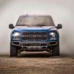 A blue 2020 Ford Raptor is shown from the front driving through a dirt cloud near Cincinnati.