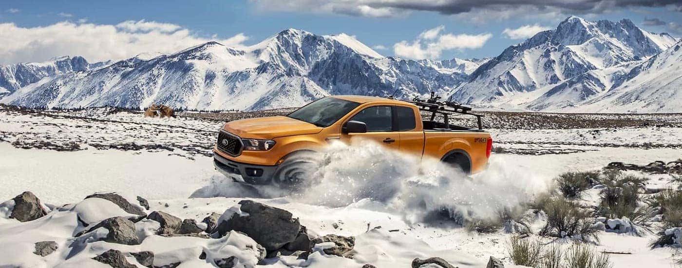 An orange 2021 Ford Ranger is driving in the snow in front of distant mountains.