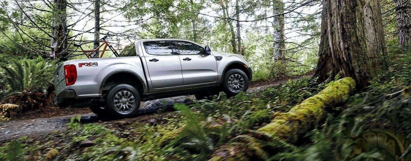 A silver 2021 Ford Ranger is driving through a woodland trail with a bike in the bed.