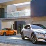 A white 2021 Ford Mustang Mach-E Hybrid is parked next to an orange 2021 Ford Mustang.