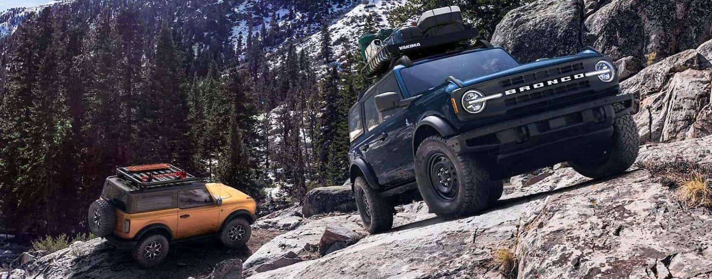 An orange 2021 Ford Bronco 2-door and a blue 4-door are parked on a rocky mountain side after winning the 2021 Ford Bronco vs 2021 Toyota 4Runner comparison.