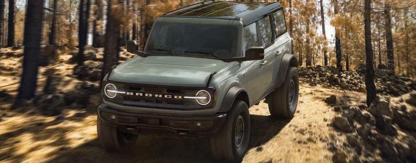 A green 2021 Ford Bronco 4-door Wildtrack is shown from the front while driving on a woodland trail.