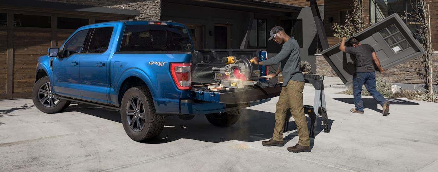 Contractors are working in front of a modern home and in the bed of a blue 2021 Ford F-150.