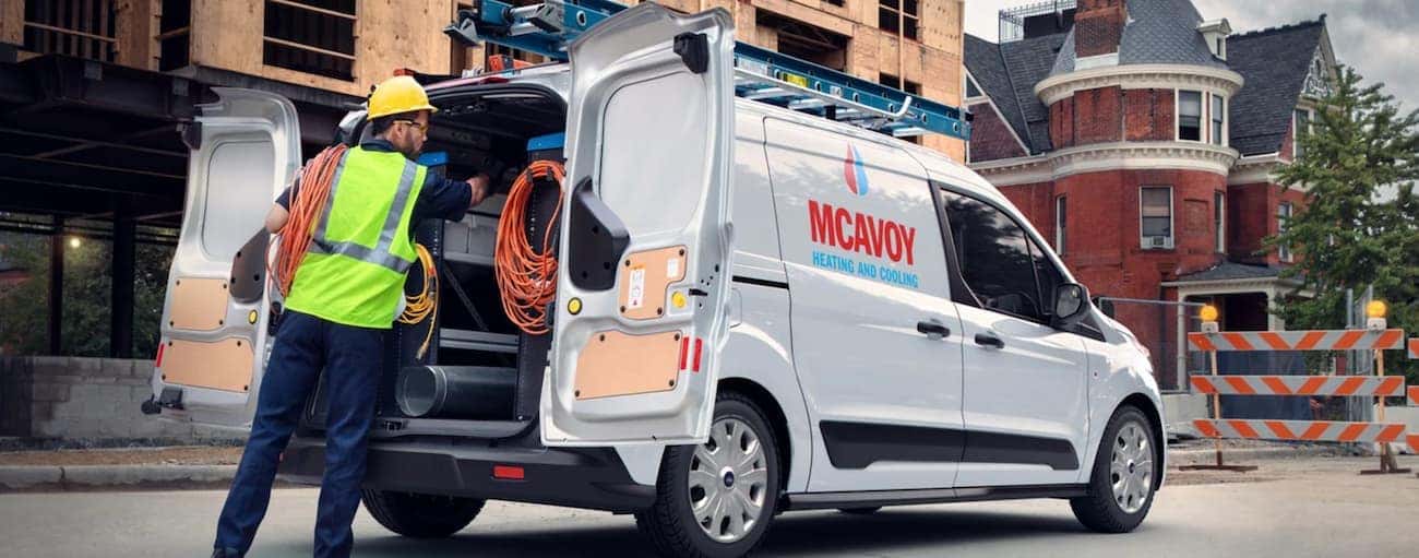 A worker is taking gear out of the back of a 2021 Ford Transit Connect with a logo.