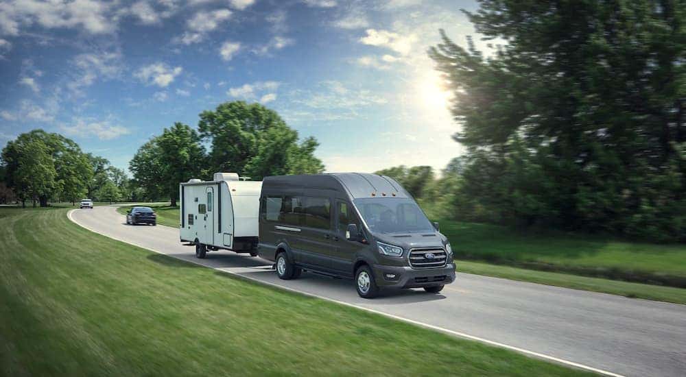 A grey 2020 Ford Transit is towing a white trailer down the road.