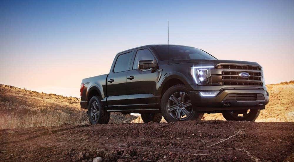 A black 2021 Ford F-150 is parked on a dirt pile at dusk.