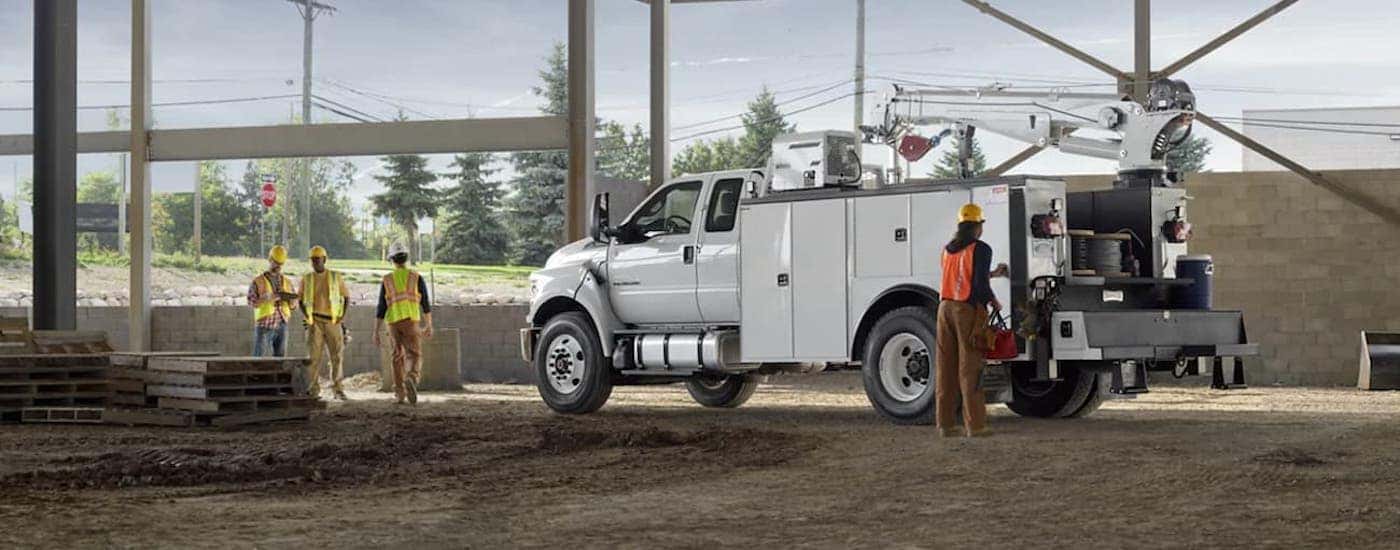 A white 2021 Ford F-750 is parked next to workers at a construction site.