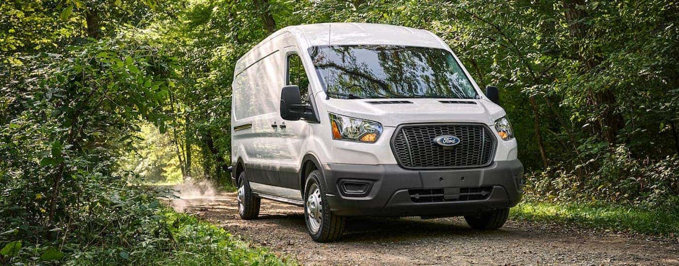 A white 2021 Ford Transit is driving on a dirt road after leaving a Ford commercial vehicle dealer.