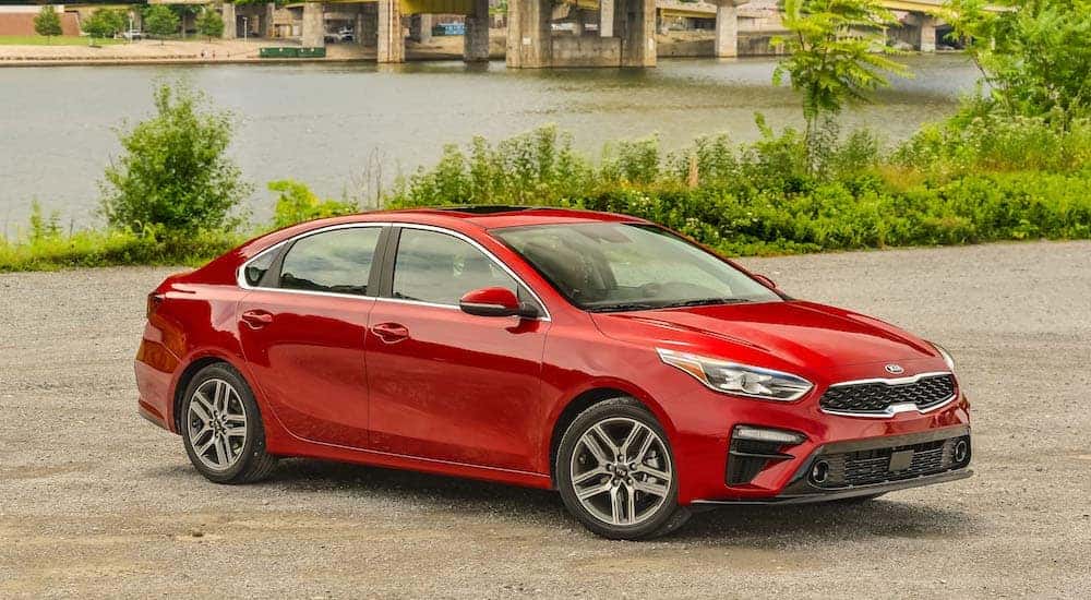 A popular used car, a red 2019 Kia Forte, is parked on the pavement with a river in the background.