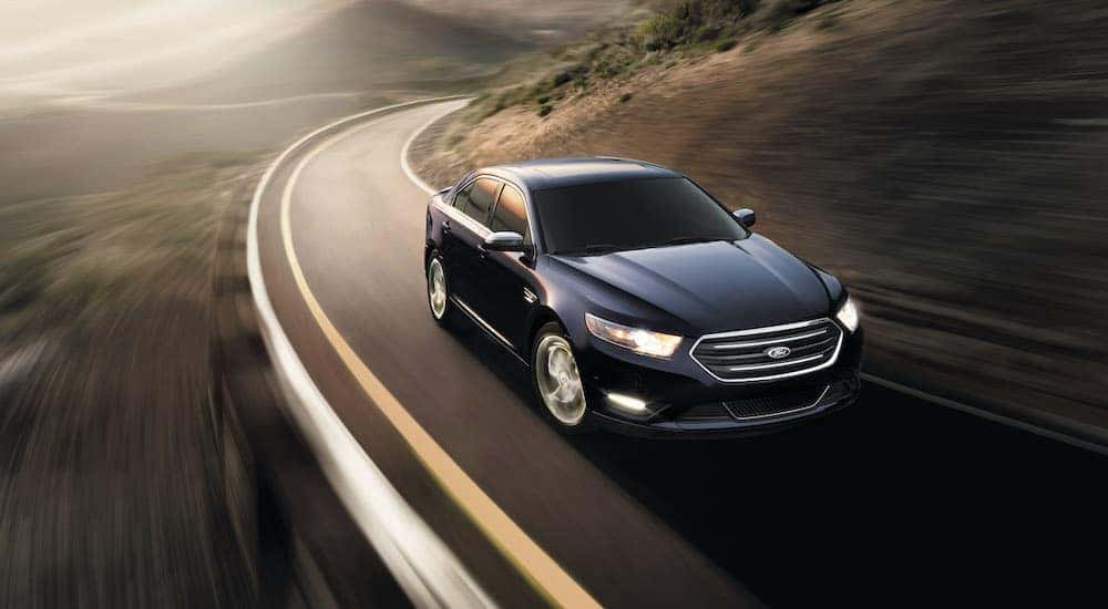 A popular used Ford for sale, a dark blue 2012 Ford Taurus, is driving down the highway.