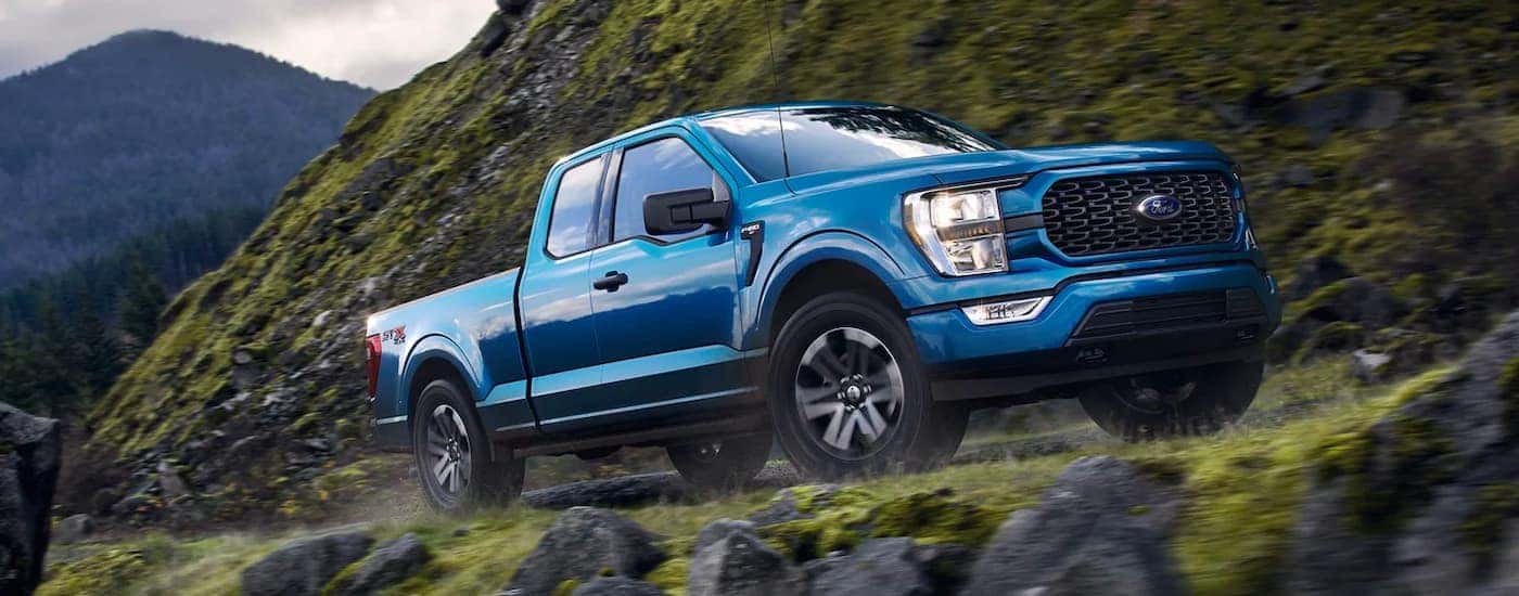 A blue 2021 Ford F-150 Hybrid is shown driving up a steep road in the mountains past mossy rocks.