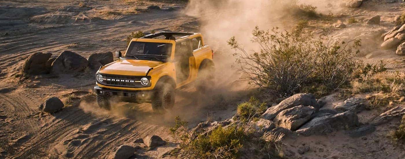A yellow 2021 Ford Bronco 2-Door is off-roading on a dusty dirt trail.