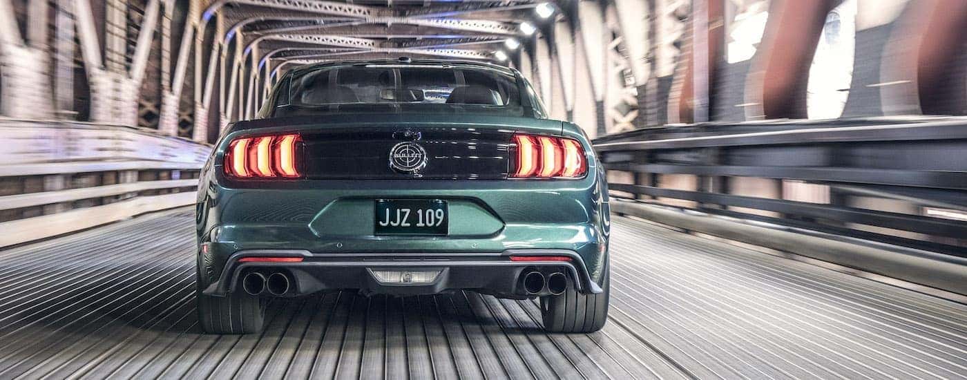 A green 2019 Ford Mustang Bullitt is shown from the rear driving on a bridge.