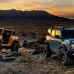 An orange and a blue 2021 Ford Bronco are parked in a desert at sunset.
