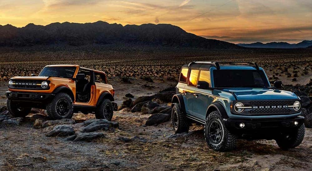 An orange and a blue 2021 Ford Bronco are parked in a desert at sunset.