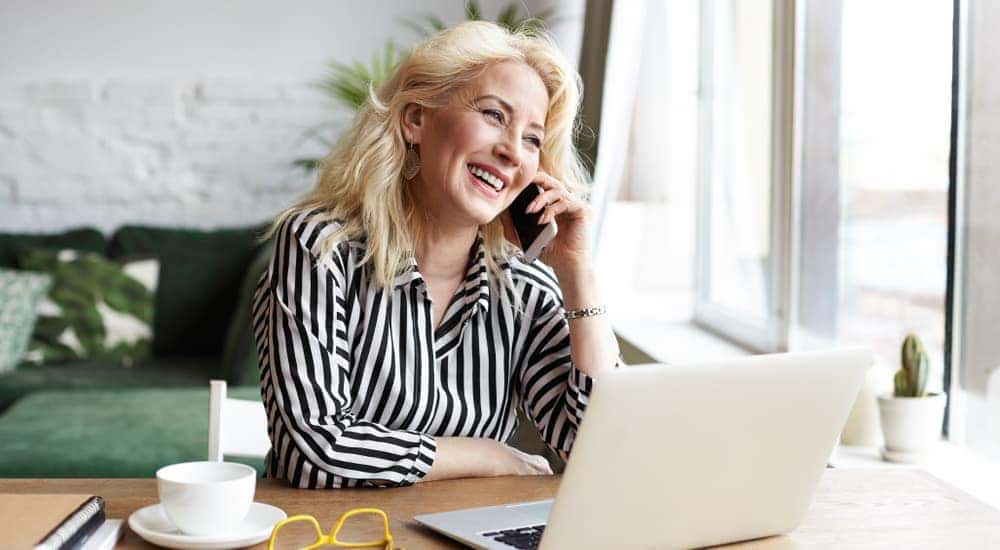 A woman is on the phone and using her laptop.