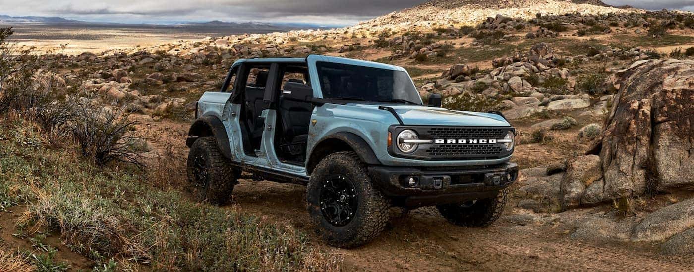 A light blue 2021 Ford Bronco 4-Door with no door is on a desert trail.