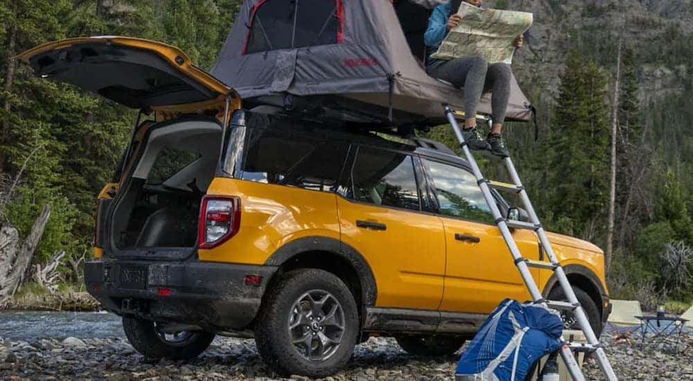 A woman is looking at a map while in a tent on top of a yellow 2021 Ford Bronco Sport from an Ohio Bronco dealer.