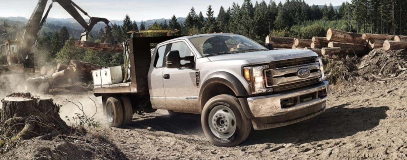 Lumber is being loaded onto a silver 2018 Super Duty Chassis Cab at a logging site.